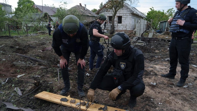 A Ukrainian police officer and war crime prosecutor inspect fragments...