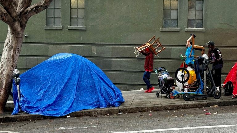 People walk by a tent set up on a sidewalk...