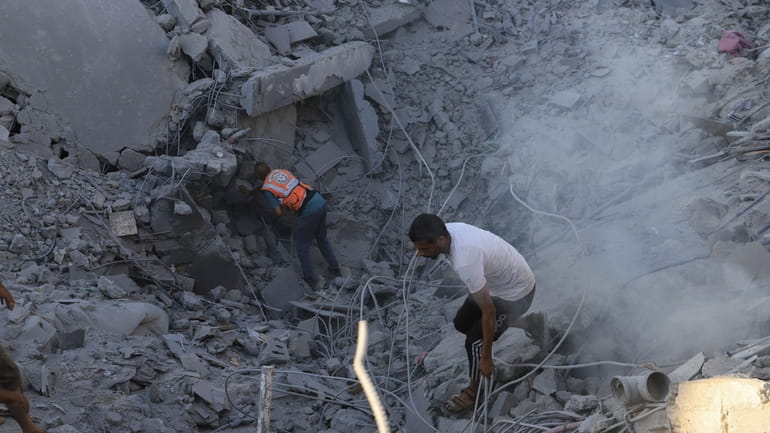 Palestinians search for bodies and survivors in the rubble of...