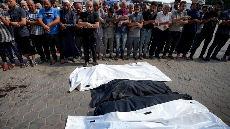 Palestinians pray next to the bodies of their relatives killed...