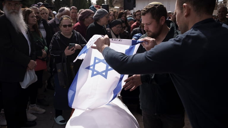 Relatives of Yitzhak Zeiger place an Israeli flag over his...