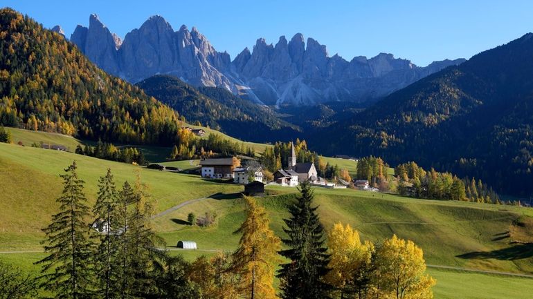 Colorful trees stand around a church at the Dolomites mountains...