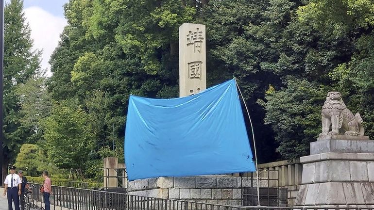 A blue sheet covers a stone pillar on which graffiti...