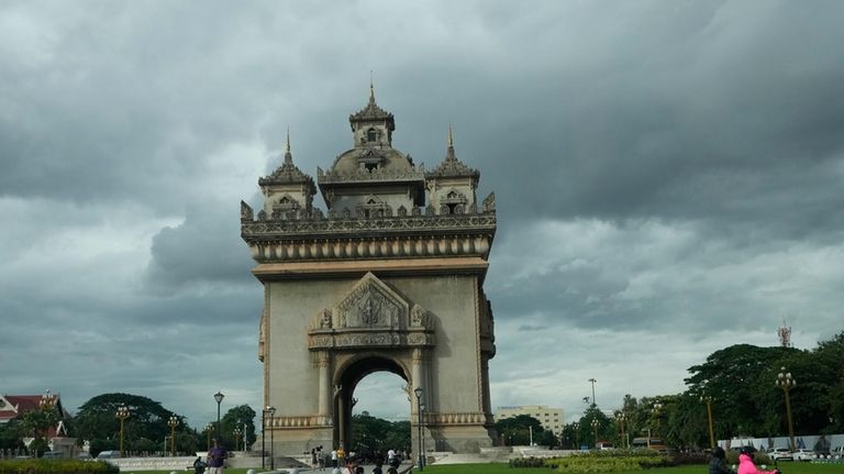 Motorcycle drivers pass the Patuxay victory monument in Vientiane, Laos,...