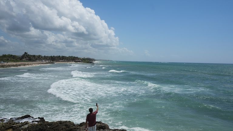 A man takes a video tfrom the rocky shore of...